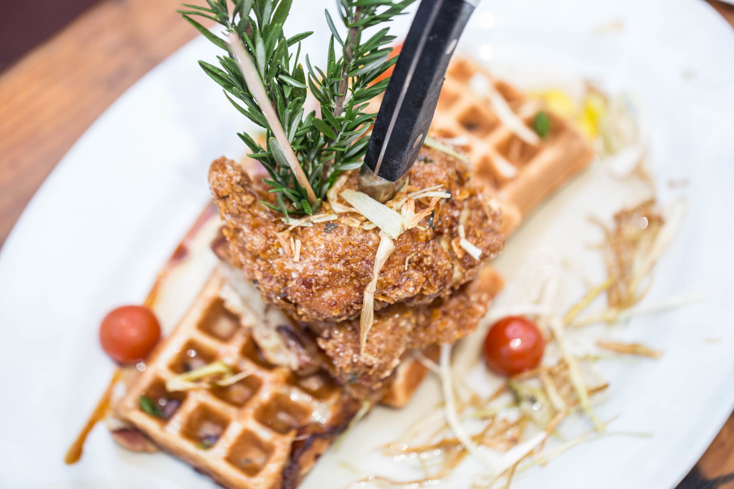Fried chicken atop waffles garnished with rosemary and drizzled with syrup, highlighting mouthwatering food presentation for brand engagement.