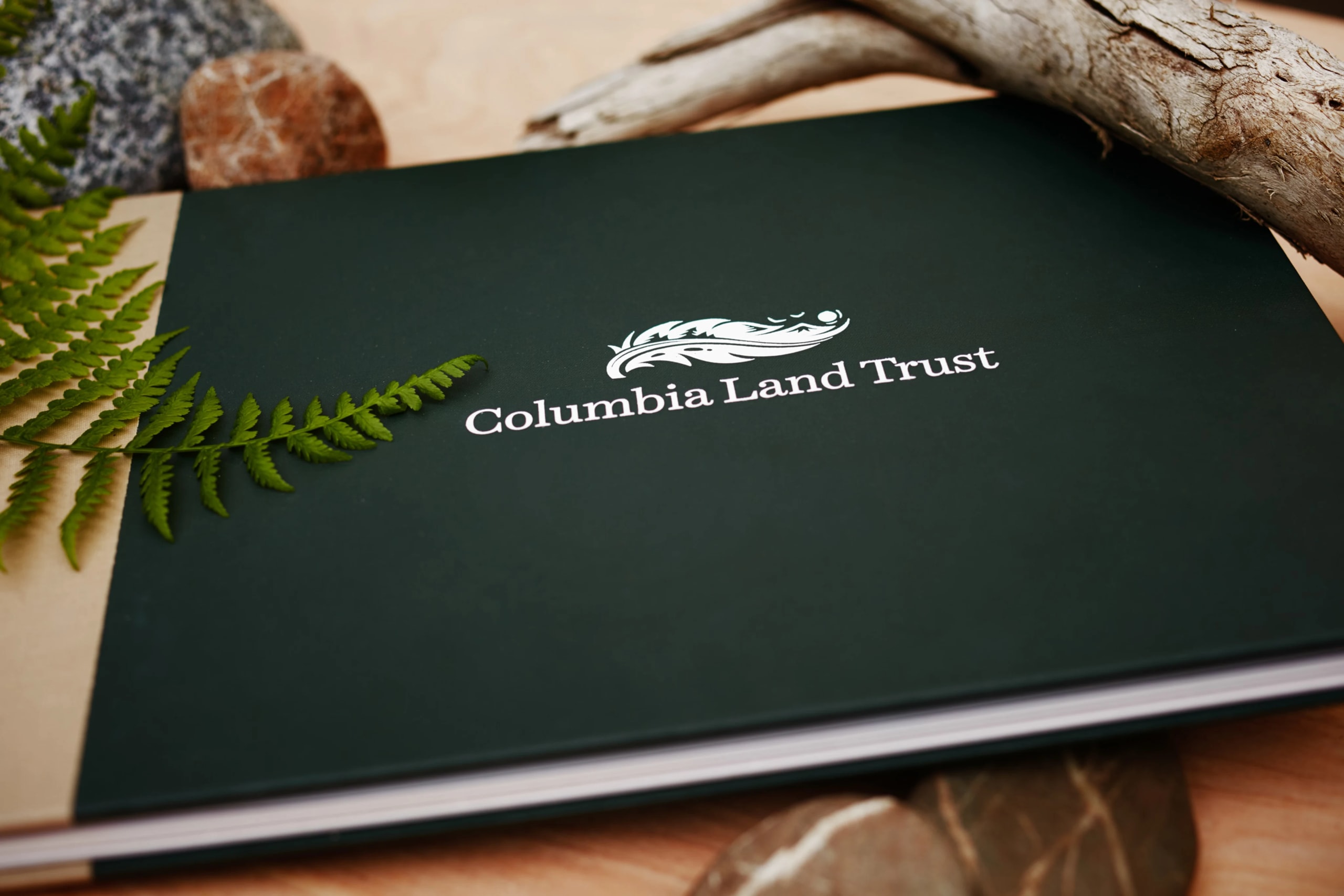 Columbia Land Trust visual identity featuring logo on dark green cover with fern and natural elements, reflecting Pacific Northwest branding by Murmur Creative.