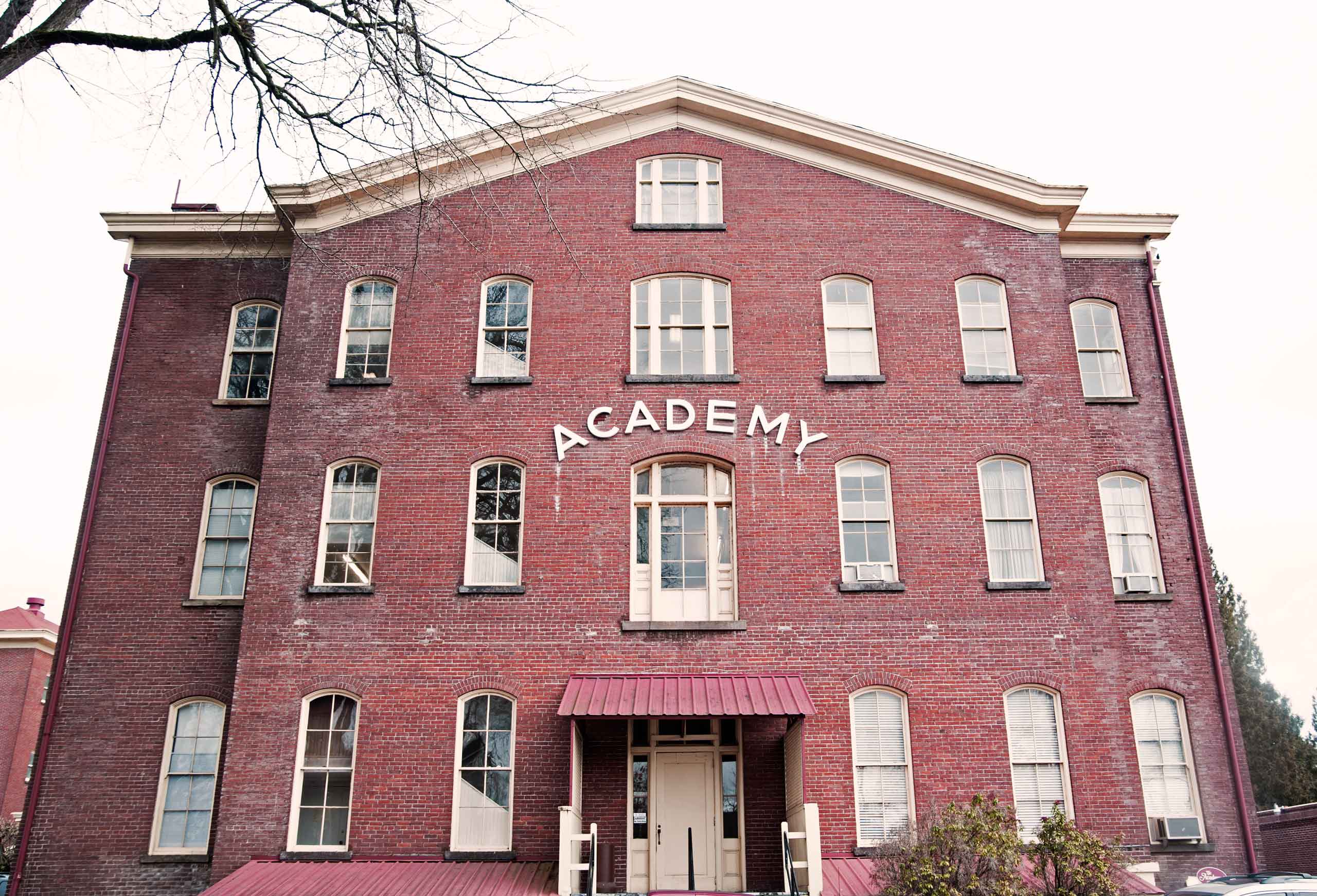 Red brick building with large windows and "ACADEMY" sign, serving as the Art of Makeup school for professional makeup artistry education.