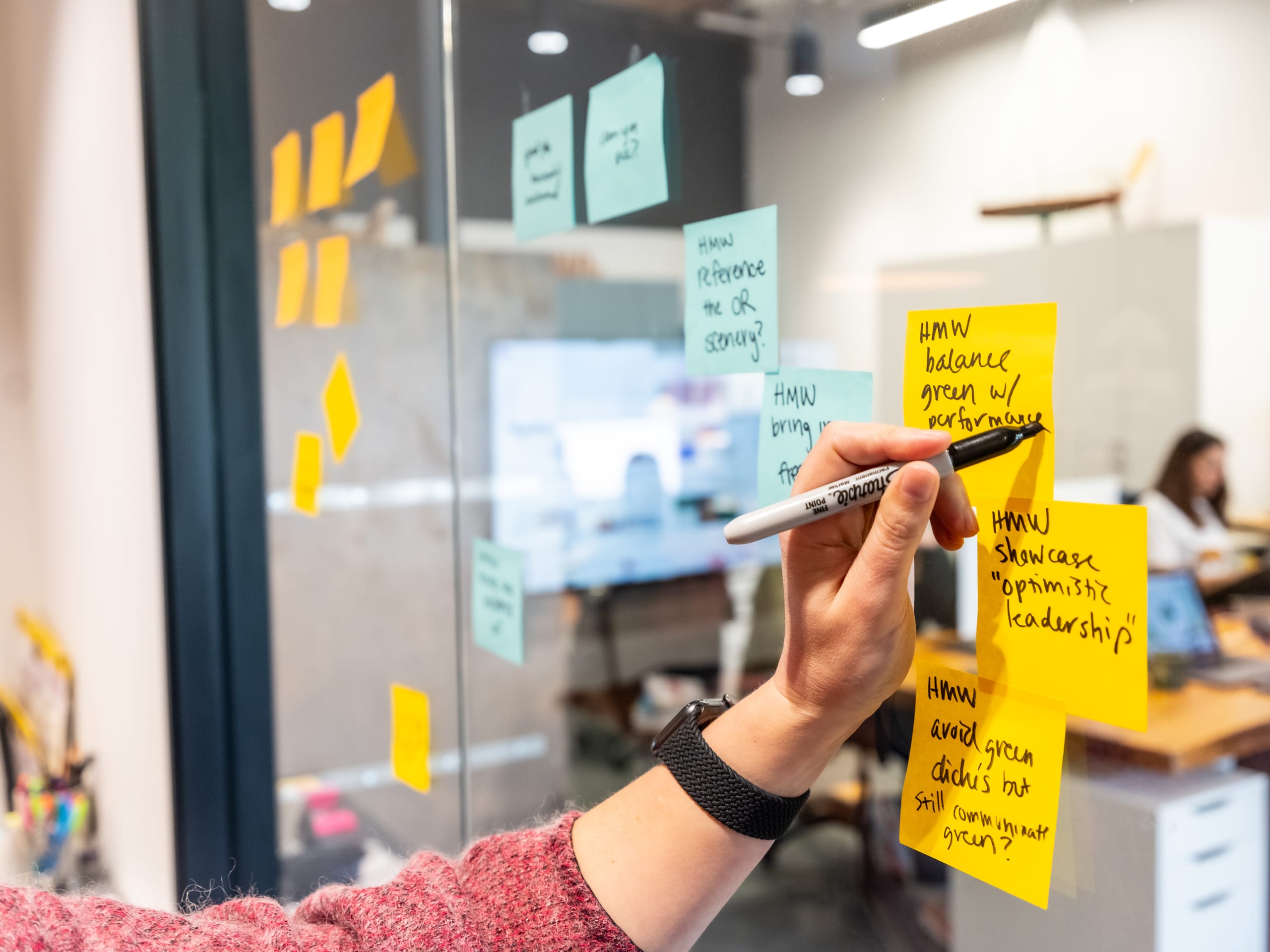 Person writing on sticky notes attached to a glass wall, brainstorming ideas for branding strategy, with emphasis on effective naming and taglines for businesses.