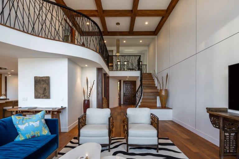 Double-height living room with a curved iron staircase railing and beamed ceiling