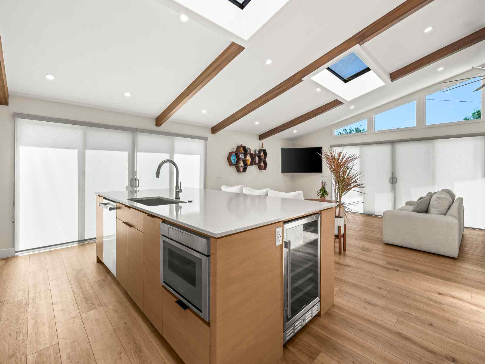 Open-concept transitional kitchen by Murray Lampert with a white oak island, wood ceiling beams, skylights, and a microwave drawer and wine refrigerator built into the island