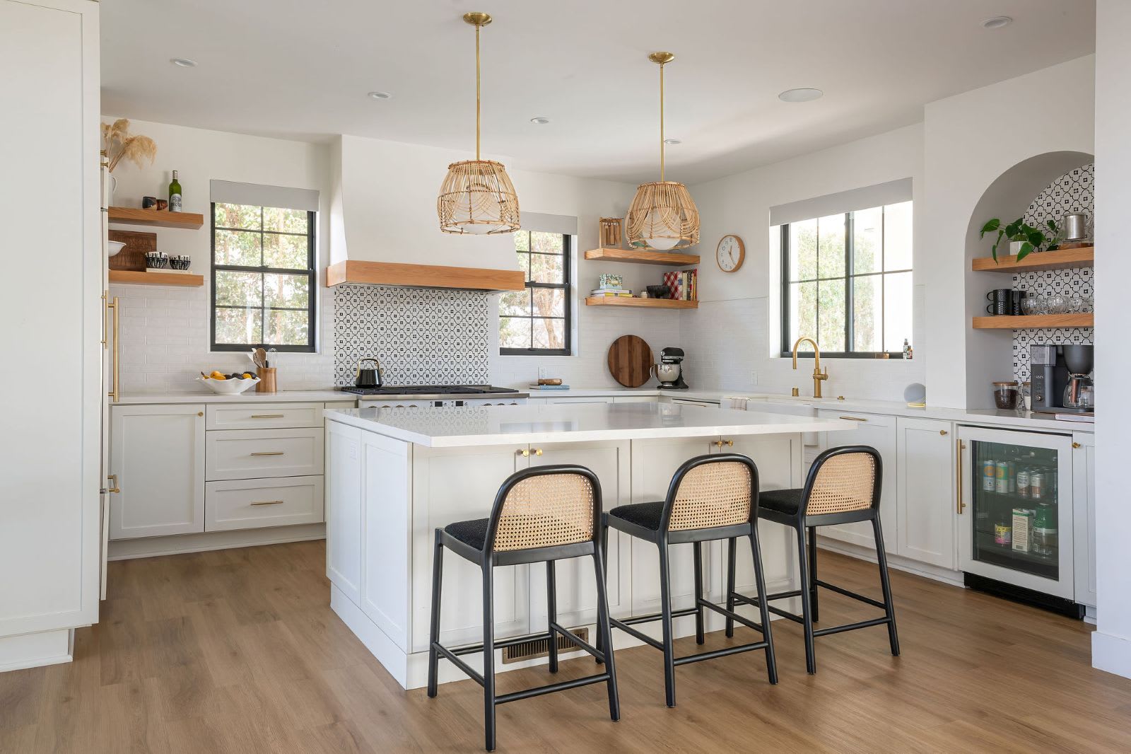 Bright white kitchen by Murray Lampert with a large island with seating for three, woven pendant lights, floating wood shelves, and an undercounter beverage refrigerator