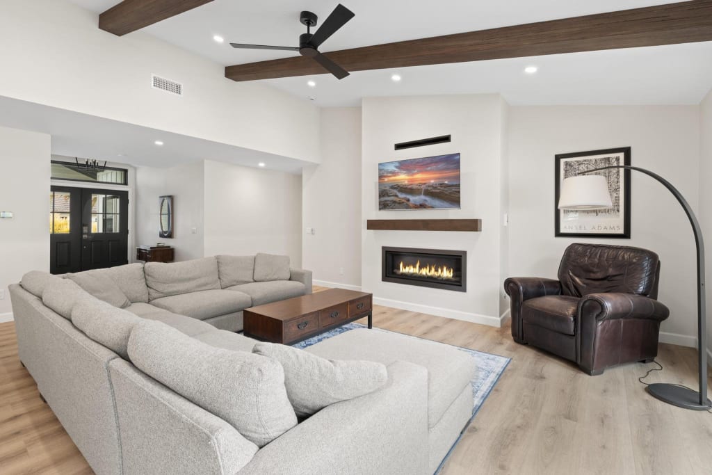 Living room looking toward black double entry doors with a transom, beamed ceiling and fireplace wall