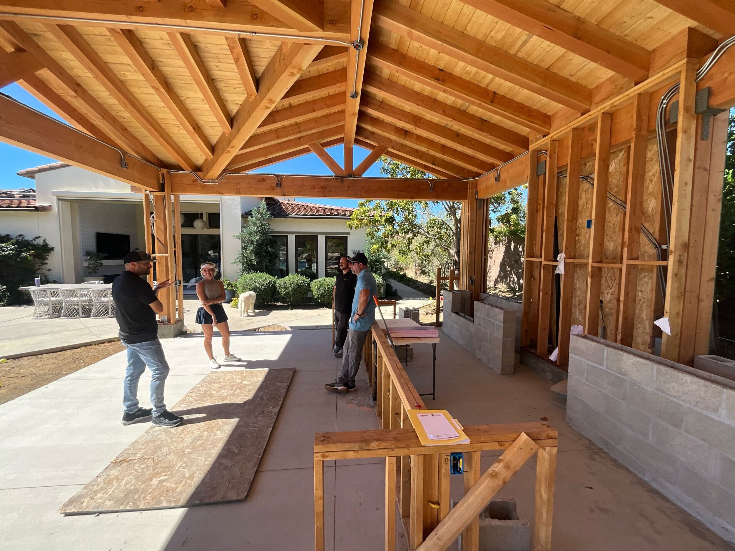 Murray Lampert team reviewing plans with homeowners during a permitted outdoor structure renovation in San Diego - exposed framing, conduit, and structural members visible