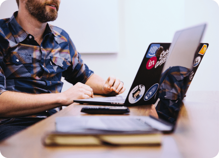 Image of a bearded man typing on a laptop with another laptop in the foreground