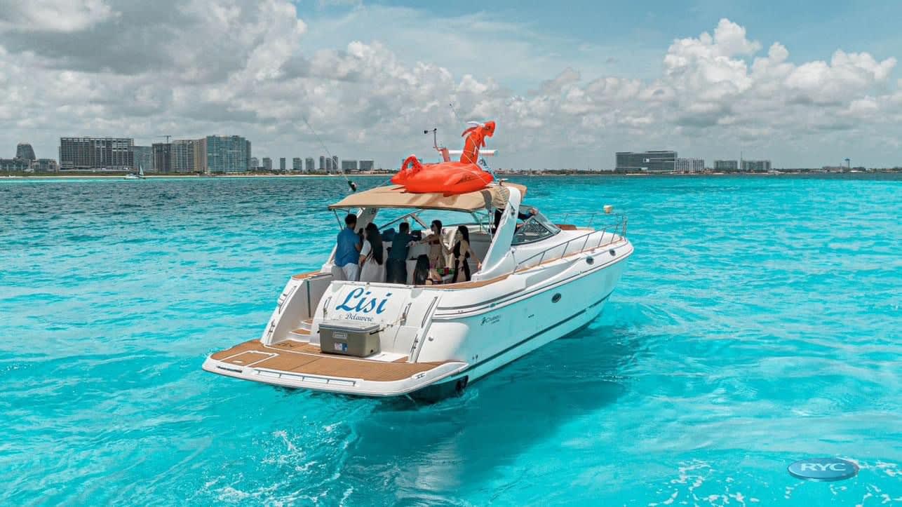A luxury yacht named 'Lisi' anchored in stunning turquoise waters near the Cancun hotel zone skyline. A group of professionals is relaxing on board, showcasing a premier option for MICE post-event celebrations, client entertainment, or luxury incentive travel.