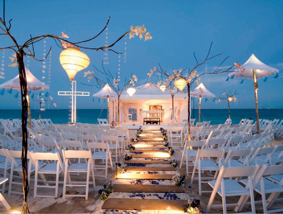 Close-up of a luxurious event table setting with gold charger plates, elegant stemware, gold Chiavari-style chairs, and white rose centerpieces. Showcases high-end equipment and chinaware rentals suitable for VIP MICE luncheons, executive dinners, or formal conference receptions in Cancun.