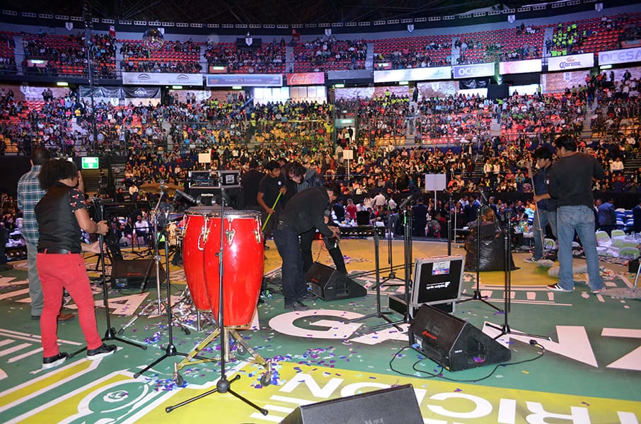 An aerial artist performing an acrobatic routine, hanging from a yellow rope high above a crowd at a corporate gala or large-scale incentive event. The stage lighting and truss system are visible, highlighting the dramatic live entertainment and event production elements provided for a spectacular MICE function.