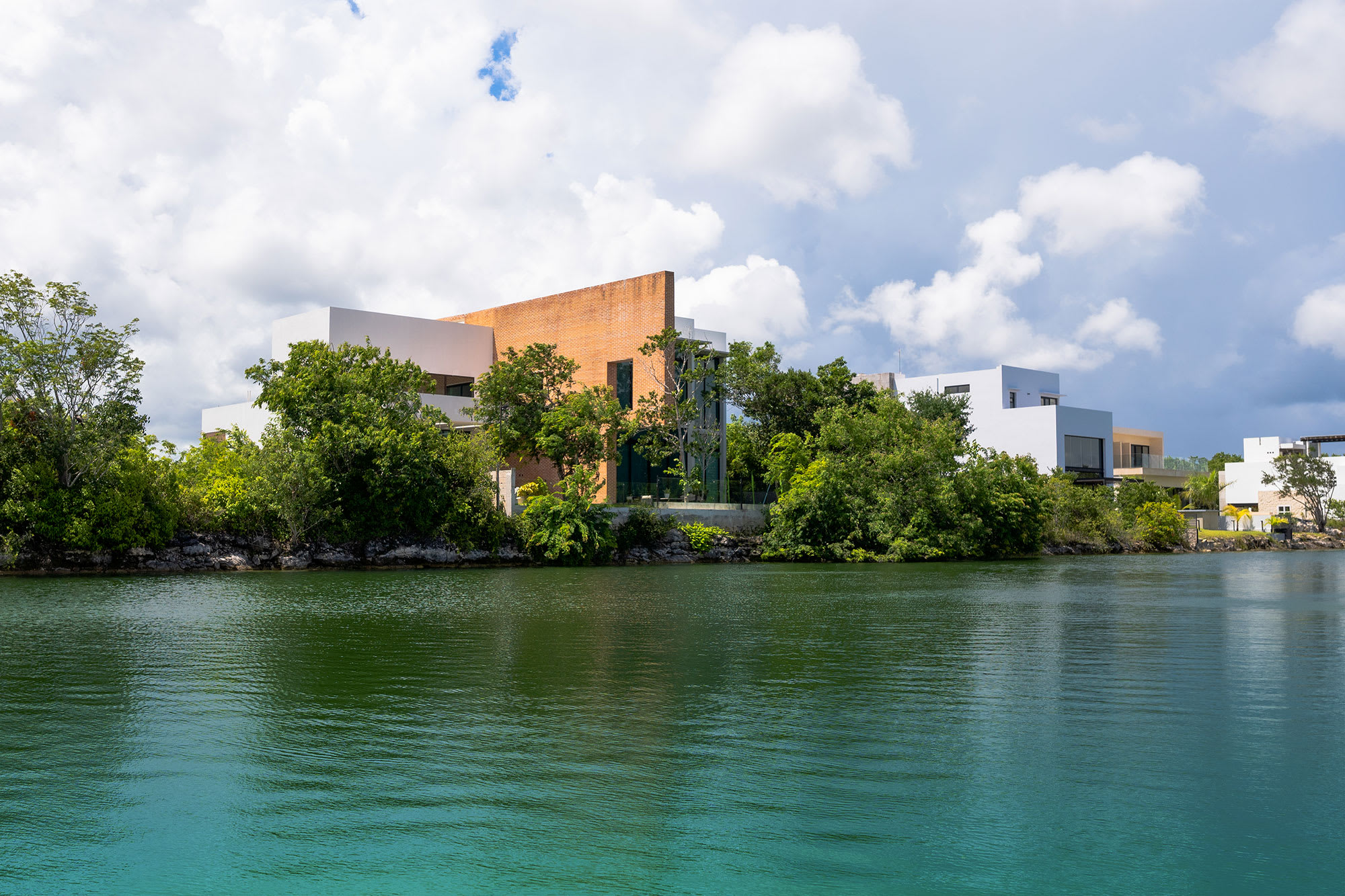 Modern, luxurious executive villas or residential buildings with unique architecture, situated along a clear turquoise waterfront, ideal for high-end executive incentive stays or VIP events in the Cancun MICE destination.