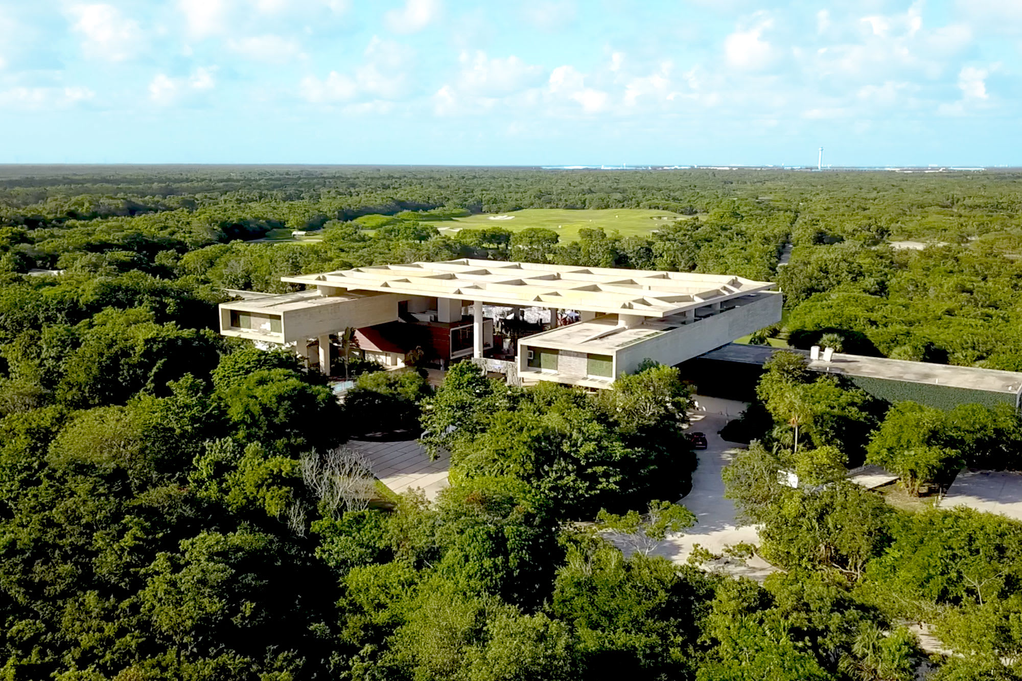 Aerial view of a stunning modern resort or club house complex surrounded by lush, dense tropical forest and a golf course in the background, promoting luxury incentive trips and executive retreats in the MICE destination