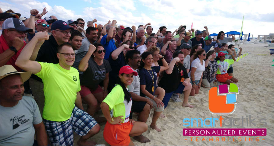 A diverse group of corporate professionals posing together on a white sand beach during a team-building event organized by Smartactiks, ideal for MICE industry incentive travel and large-scale corporate retreats in Cancun.