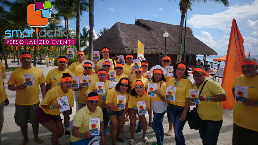 A large corporate group in matching yellow shirts and orange headbands participating in a beach team-building activity organized by Smartactiks for the MICE industry in a tropical coastal destination.