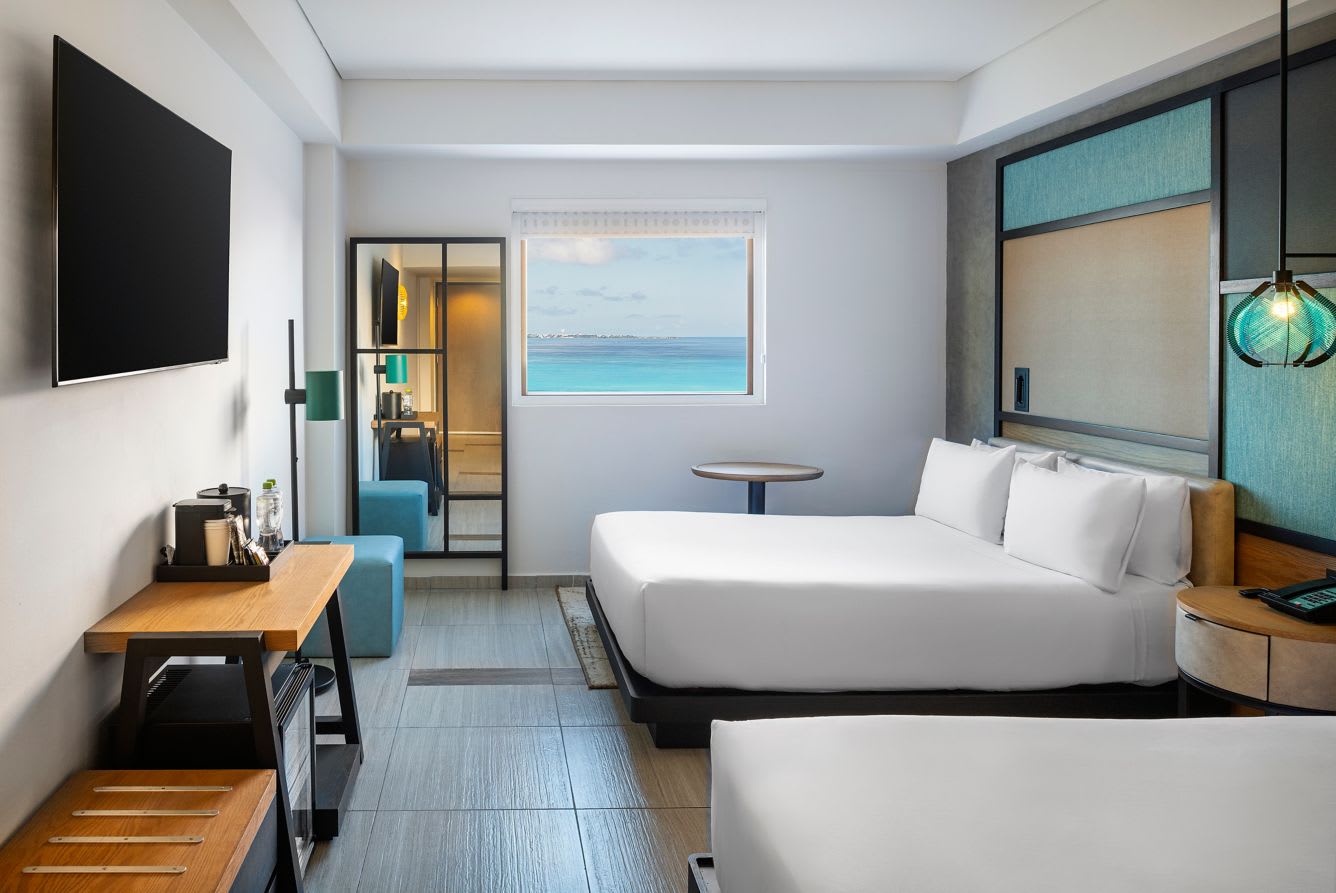 Modern ocean-view hotel room in Cancun with two comfortable queen beds, work desk, flat-screen TV, coffee station, and stunning Caribbean Sea views. Ideal accommodation for MICE attendees, conference delegates, incentive trip participants, and business travelers seeking relaxation after meetings and events.
