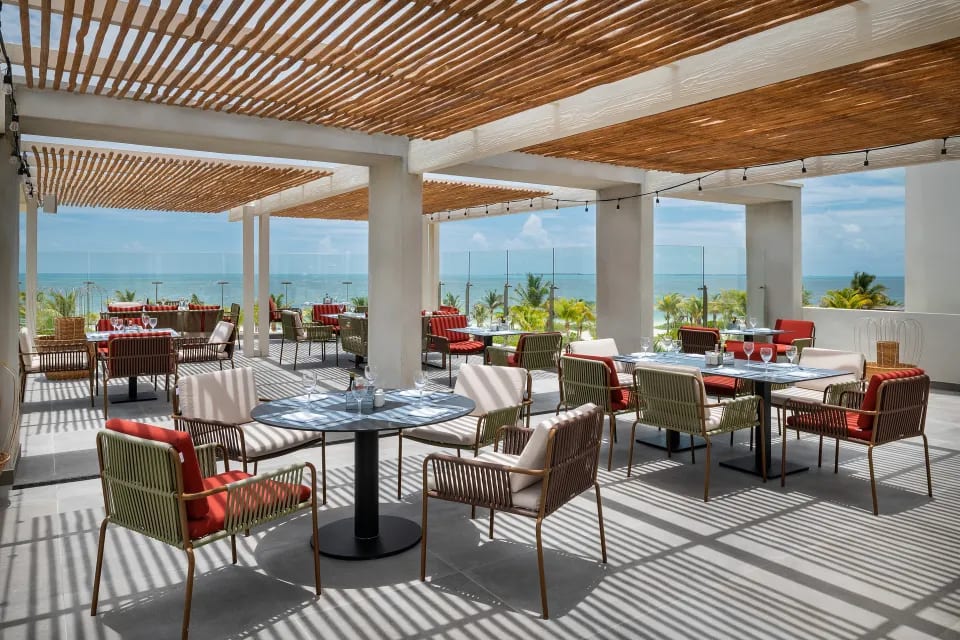 Outdoor dining at the BLoved restaurant terrace in Catalonia Grand Costa Mujeres, showcasing oceanfront views and modern seating ideal for corporate gala dinners, MICE networking events, and incentive travel group meals in the Mexican Caribbean.