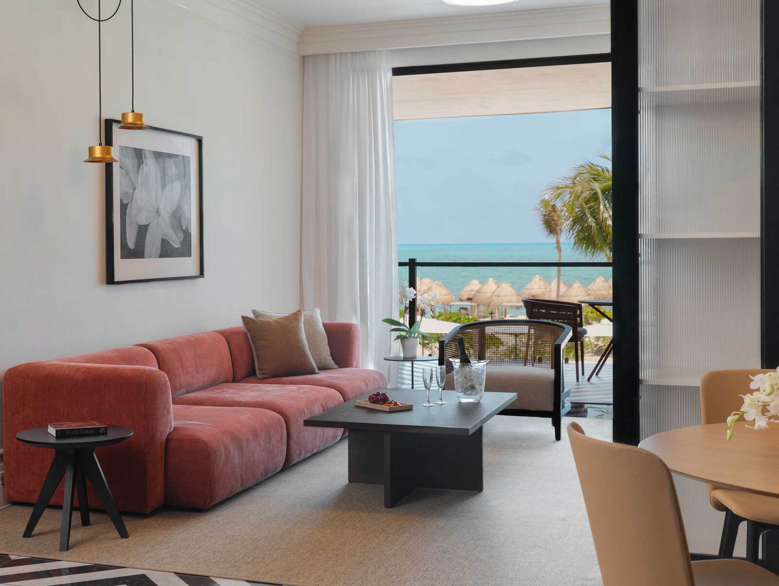 Elegant oceanview suite living area in a luxury Riviera Maya resort, featuring a modern pink sofa, contemporary furniture, champagne setup, and floor-to-ceiling sliding doors opening to a private balcony with direct Caribbean Sea and beach views – premium executive accommodation for MICE events, corporate conferences, incentive trips, meetings, and high-level business retreats in Mexico.