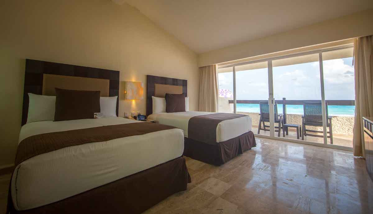 A modern guest room at Grand Park Royal Cancun featuring two comfortable beds and a private balcony with turquoise Caribbean views. This luxury accommodation is ideal for MICE industry delegates, incentive travel winners, and corporate travelers seeking premium amenities and a relaxing environment during business events in Cancun.