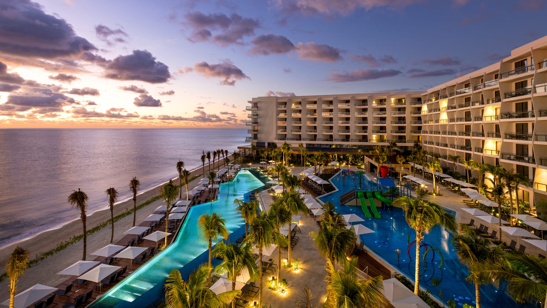 Elevated sunset view of the Hilton Cancun, an All-Inclusive Resort, showing illuminated pools and modern architecture. An inspiring setting for evening MICE networking events, outdoor corporate galas, and luxury incentive travel rewards in Cancun, Mexico.