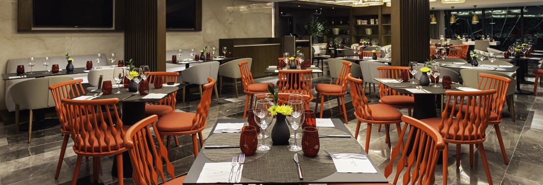 A modern, upscale hotel restaurant at the NH Collection Merida Paseo Montejo with warm, burnt-orange seating and sleek gray tables, set for fine dining. This versatile space is ideal for MICE industry functions, including group dinners, corporate event, networking receptions, and conference lunches. #MICE, #hotel #dining, #groupevents, #corporatemeetings, #networking #space, #conference #venue, #incentivetravel, Yucatán, Merida.