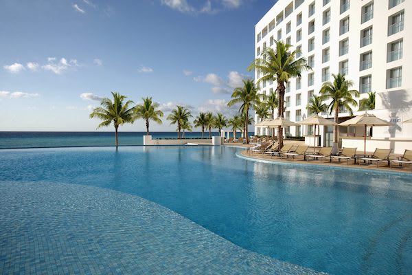 Wide-angle view of the luxury infinity pool at Le Blanc Spa Resort Cancun, highlighting an expansive outdoor space for corporate networking cocktails, MICE incentive group activities, and high-end brand activations overlooking the Caribbean Sea