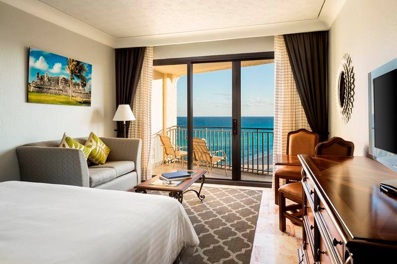 An interior view of a luxury guest room at Marriott Cancun Resort featuring a private balcony with ocean views, a comfortable seating area, and elegant decor, ideal for high-end corporate incentive travel and executive accommodation for international business events.