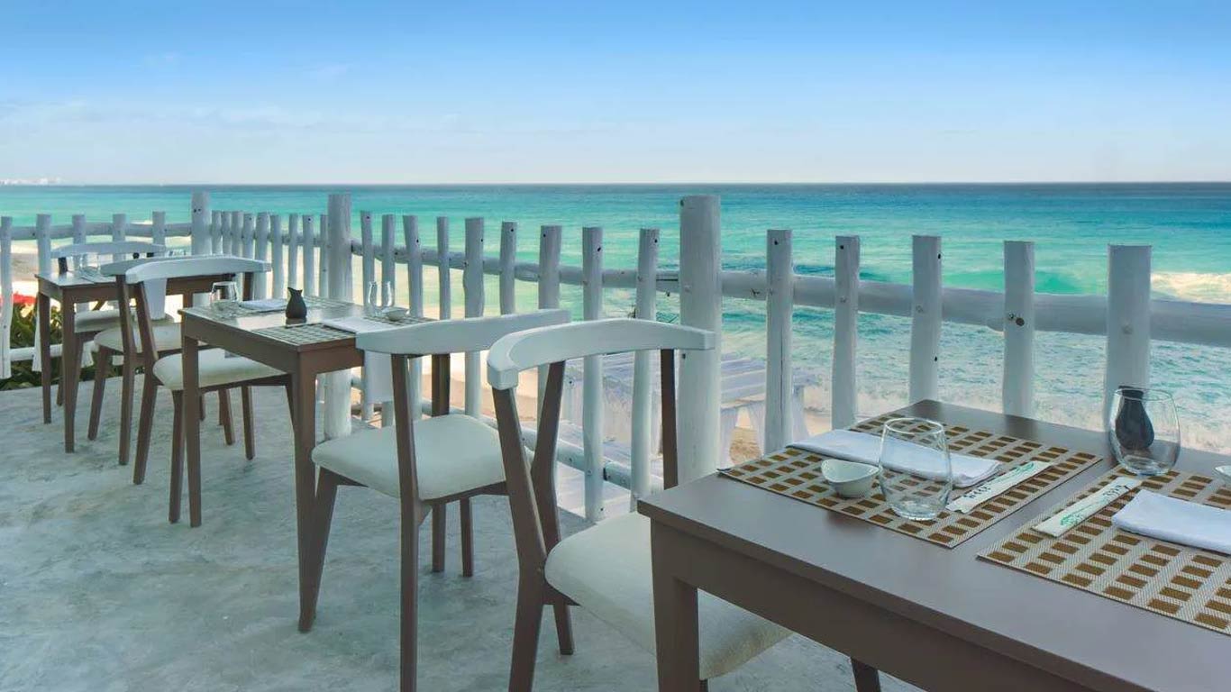 An outdoor oceanfront dining terrace at Mía Cancún Resort featuring contemporary wooden tables and chairs overlooking the turquoise Caribbean Sea, ideal for small corporate group dinners, executive networking sessions, and intimate MICE incentive events.