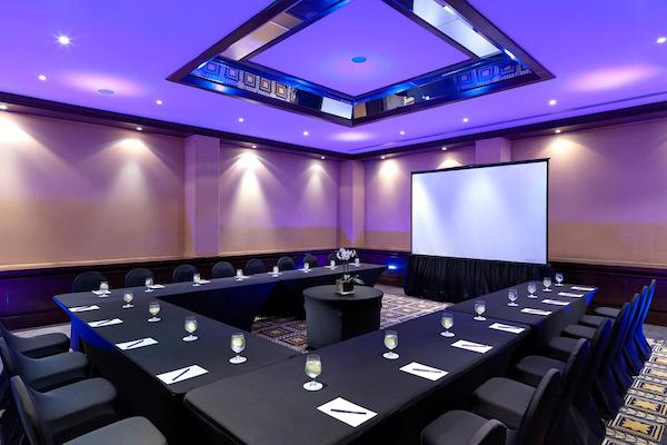 A professional U-shape conference room setup at Paradisus Cancun All Inclusive Resort & Villas, featuring black linens, a large projection screen, and modern purple LED ceiling lighting. This versatile venue is designed for MICE industry requirements, including corporate board meetings, breakout sessions, and professional seminars.