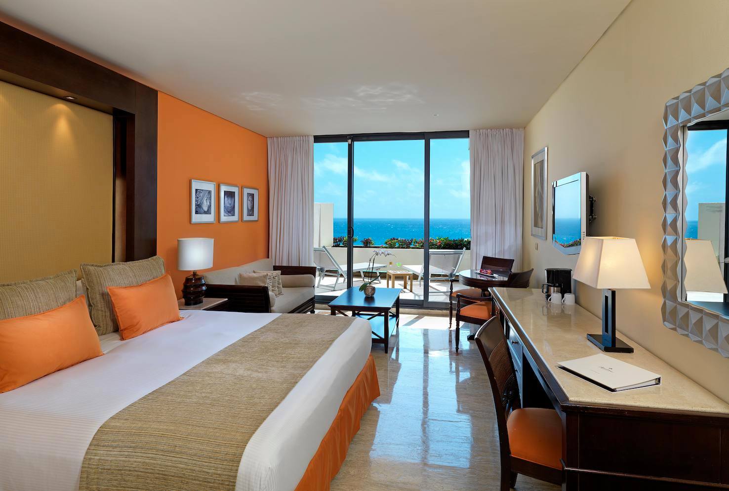 Interior of a luxury King Bedroom at Paradisus Cancun All Inclusive Resort & Villas featuring a private balcony with Caribbean Sea views, a dedicated work desk, and vibrant orange accents. Ideal for executive travelers and MICE incentive groups seeking premium accommodations during corporate conferences and international business events in Mexico.
