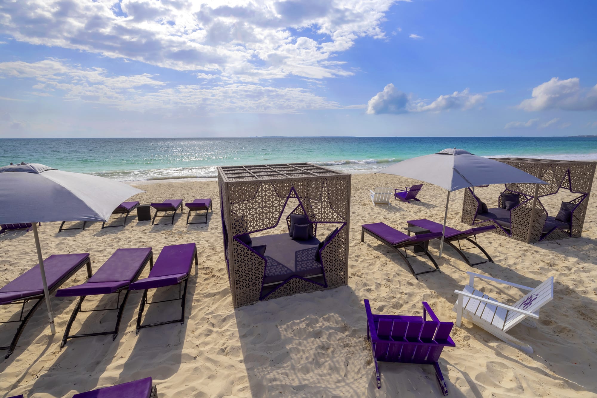 Luxury beachfront cabanas and purple lounge chairs on a white sand beach at Planet Hollywood Cancun. These premium outdoor settings are ideal for MICE industry networking events, corporate incentive travel relaxation, and private group gatherings in the Mexican Caribbean.