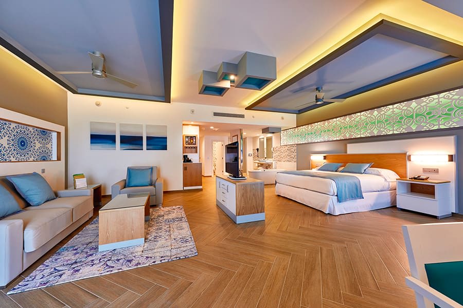 Contemporary executive guest room at Riu Palace Costa Mujeres with a king bed, blue sofa, and modern workspace, offering premium accommodations for corporate incentive groups and high-end business travel.