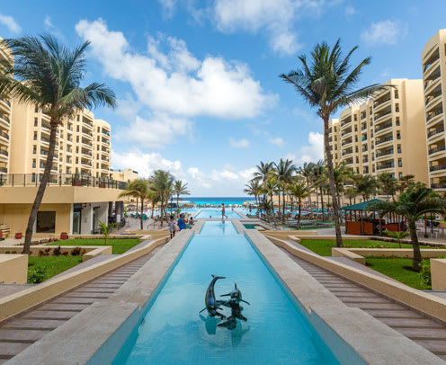 Beachfront reflecting pool with dolphin sculpture at Royal Sands Resort, ideal for MICE retreats and incentive travel. Surrounded by palm trees, modern architecture, and ocean views.