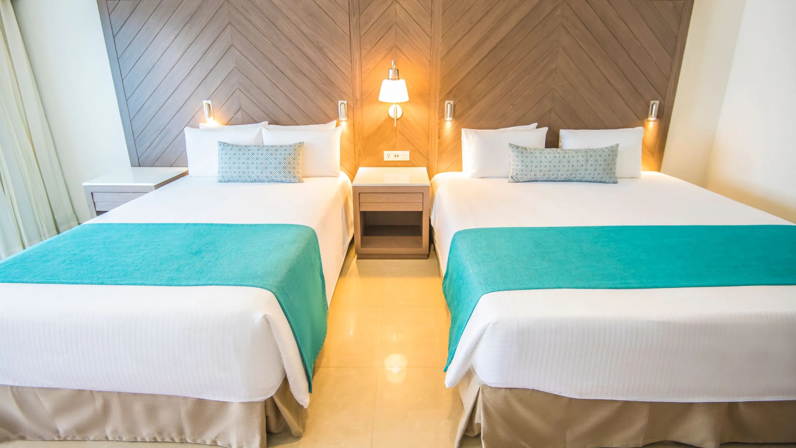 Modern double room at Sunscape Cancun Resort & Spa featuring turquoise accents, wood headboards, and functional lighting—ideal for MICE group accommodations, corporate travel, and incentive stays in Mexico.