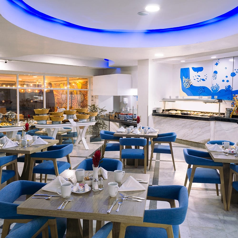 Bright and modern buffet restaurant at Sunset Royal Beach featuring blue cushioned seating, ocean-themed decor, and organized table settings—ideal for MICE group dining, incentive breakfasts, and networking meals in Cancun.
