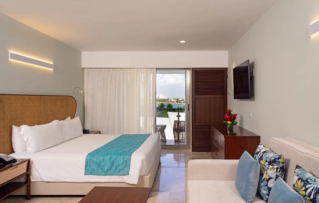 Modern guestroom at Sunset Royal Beach featuring a king bed, sofa seating, balcony with city views, and elegant decor—ideal for MICE executive stays, VIP accommodations, and incentive travel in Cancun.