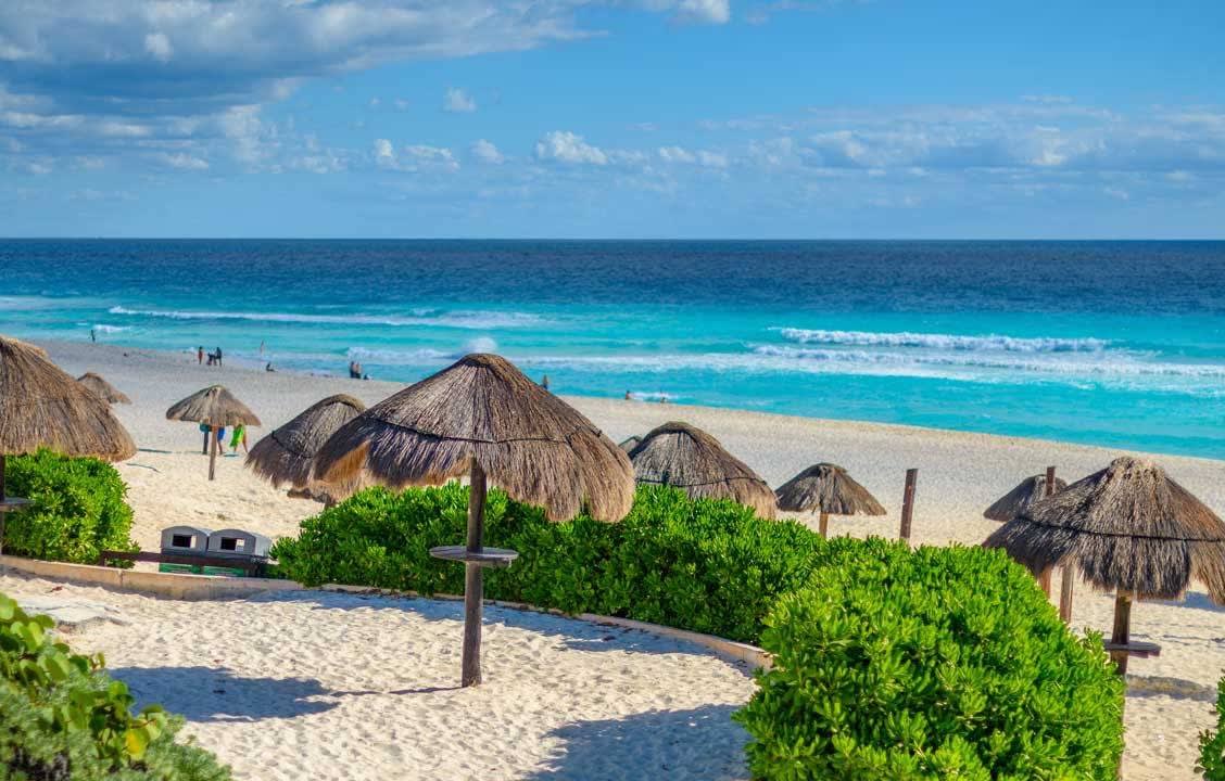 White sand beach at The Royal Cancun featuring thatched palapas, turquoise ocean waves, and tropical vegetation—ideal for MICE leisure extensions, incentive travel, and beachfront relaxation experiences in Mexico.