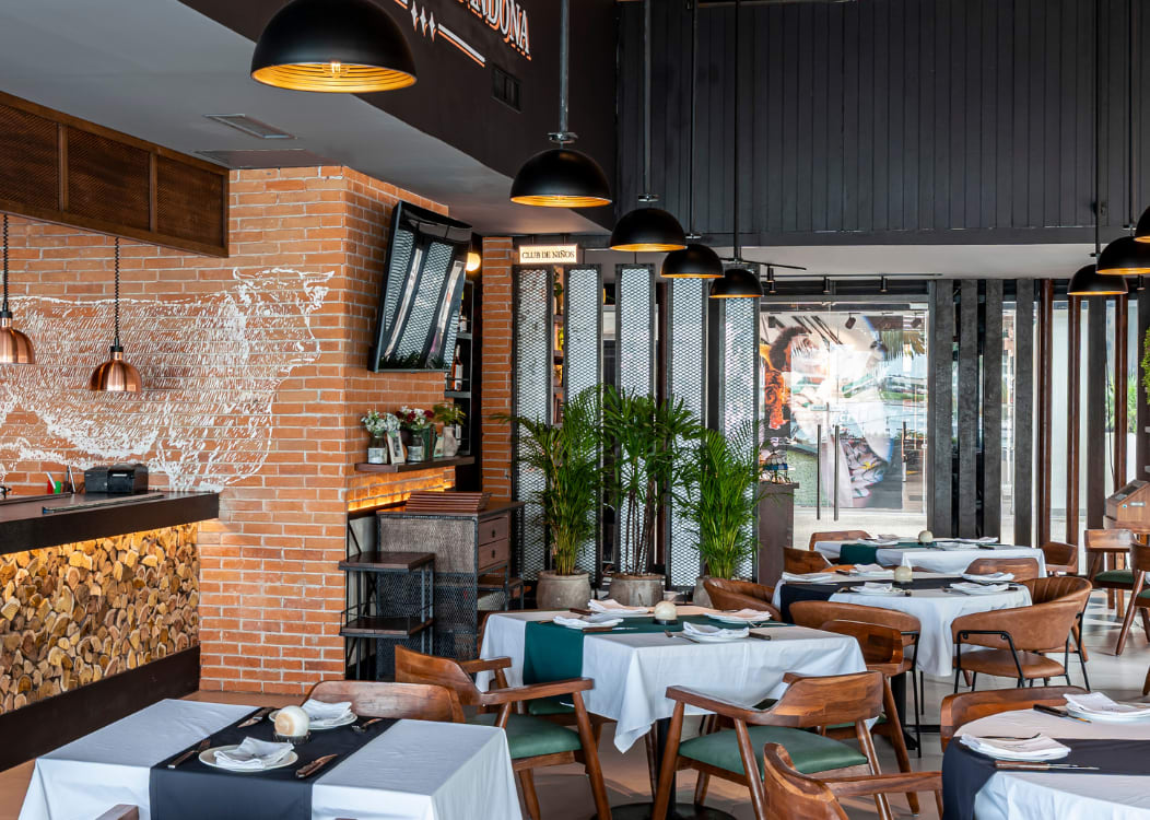 Interior view of a modern, upscale restaurant in Cancún, Mexico, featuring exposed brick, stylish black paneling, wood accents, and contemporary copper light fixtures. The dining area is set with tables ready for a MICE function, ideal for smaller group meetings, incentive travel meals, or executive networking events. The design provides a sophisticated and private atmosphere for corporate hospitality and business gatherings.
