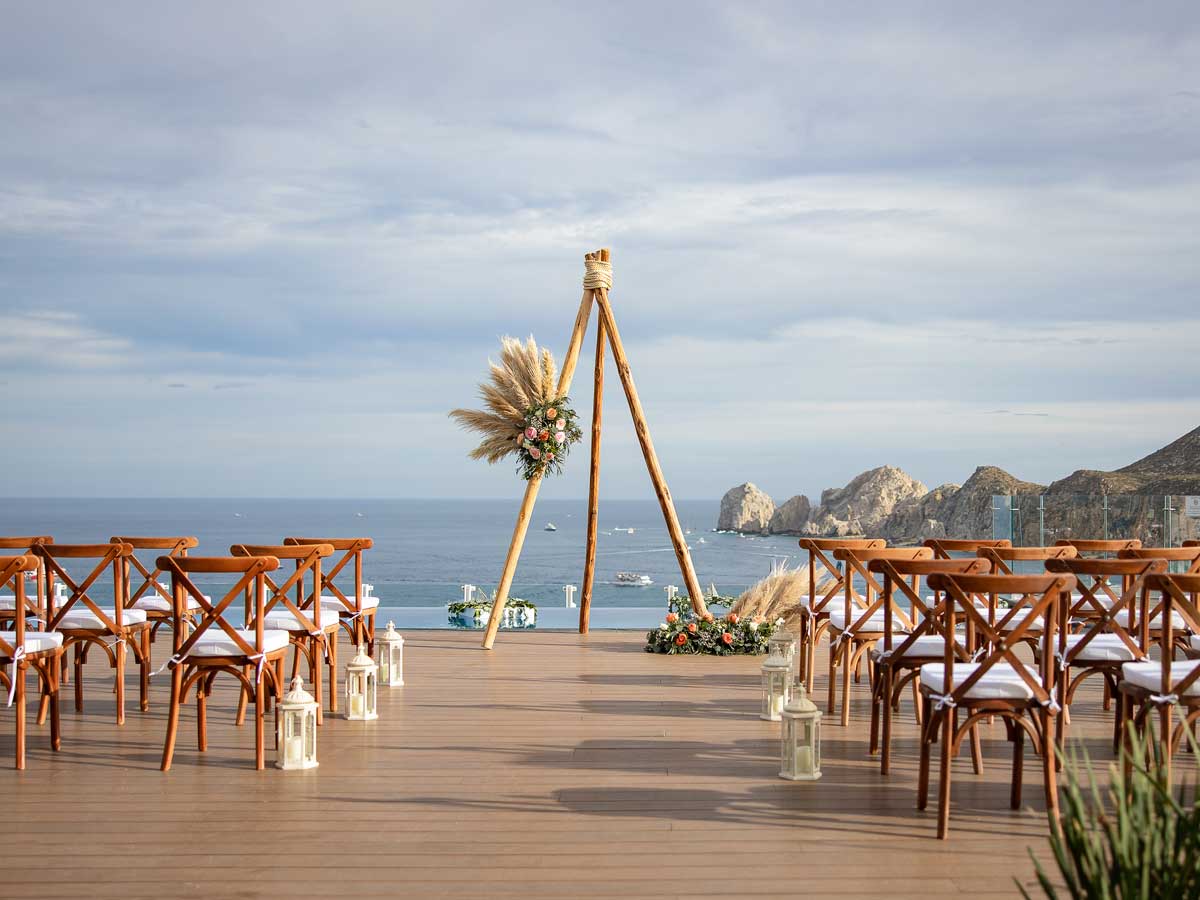 Oceanfront ceremony setup at Corazón Cabo Resort & Spa featuring wooden chairs, lanterns, and floral arch—ideal for MICE celebrations, incentive events, and destination vow renewals in Los Cabos.