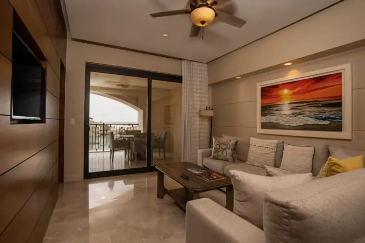Modern living room at Gran Solmar Pacific Dunes Golf & Spa featuring a beige sectional sofa, ocean-themed artwork, and balcony access—ideal for MICE executive stays, incentive travel, and VIP accommodations in Cabo San Lucas.