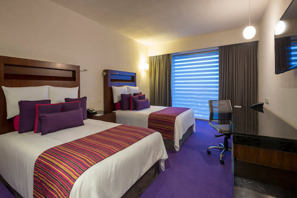 Contemporary double guest room at Camino Real Pedregal in Mexico City, featuring vibrant bedding, work desk, and natural light. Ideal for MICE travelers seeking comfort and productivity.