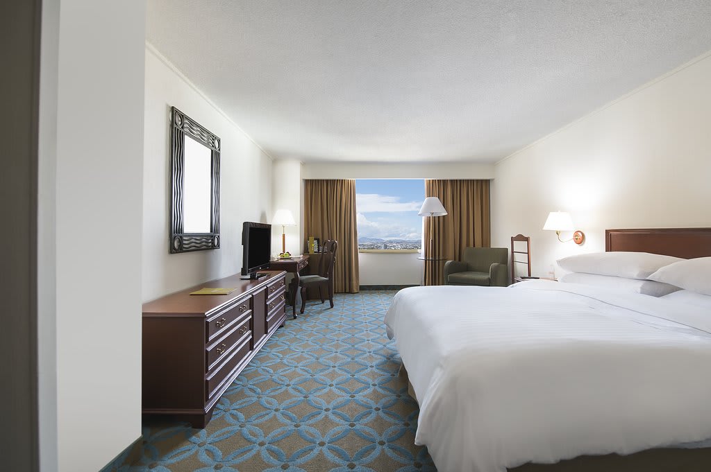 Spacious guest room at Fiesta Americana Reforma in Mexico City, featuring a large bed, work desk, and city view. Ideal for MICE attendees seeking comfort and productivity during corporate events or incentive stays