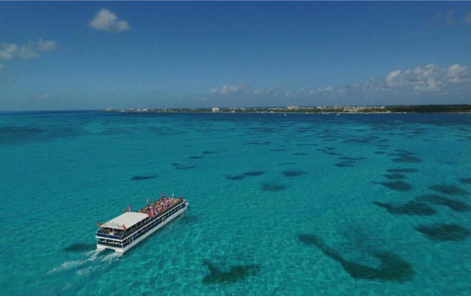 Aerial view of the large Caribbean Carnaval Catamaran sailing across the brilliant turquoise waters near Isla Mujeres, Cancun. The vessel is full of corporate group attendees, perfect for convention optional activities, team building, or a group leisure excursion during a MICE trip.