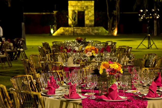 Formal nighttime event setup at Hacienda Del Rey, featuring round tables with pink and orange floral arrangements, bamboo chairs, and elegant place settings. This image showcases the spectacular outdoor venue capacity for MICE gala dinners, corporate award ceremonies, or special evening functions.