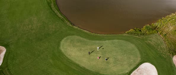 Overhead aerial view of a group of four golfers putting on a green next to a water hazard and sand bunker at Iberostar Golf Club Cancun. Excellent for incentive travel, team-building activities, and executive golf outings for the MICE industry.