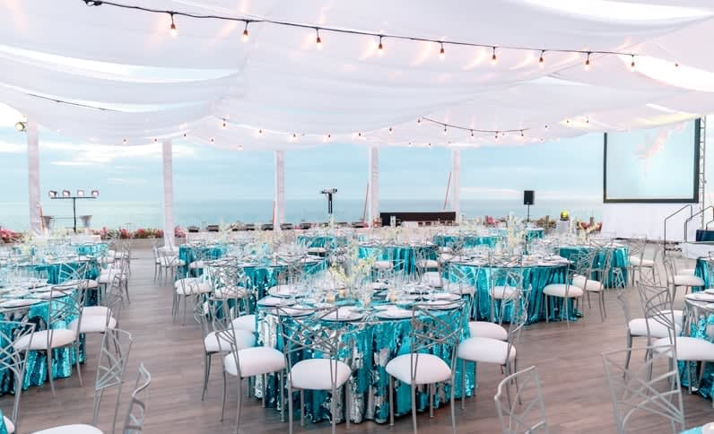 Covered outdoor event space at Grand Velas Los Cabos featuring turquoise table settings, string lights, ocean views, and AV setup—ideal for MICE galas, corporate dinners, and incentive group celebrations in Baja California Sur.