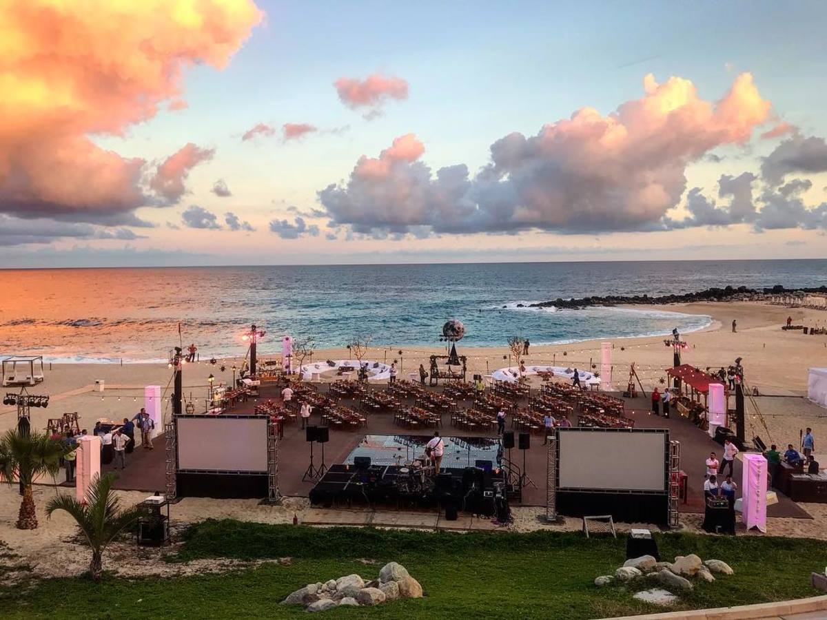 Beachfront event setup at Hilton Los Cabos Beach & Golf Resort featuring stage, projection screens, and sunset ocean backdrop—ideal for MICE ceremonies, branded activations, and corporate entertainment in Baja California Sur.