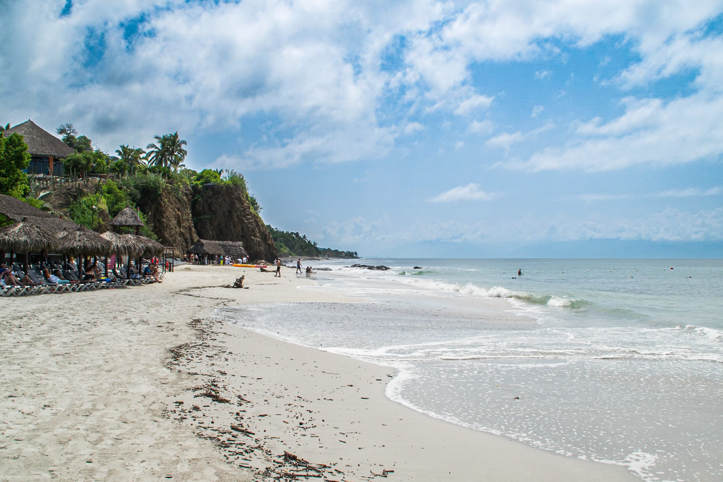 A scenic beach on the Riviera Nayarit at a luxury hotel, featuring traditional thatched palapas for breakout sessions, white sand, and gentle ocean waves, perfect for corporate events, MICE groups, and incentive travel, under a blue sky with soft white clouds