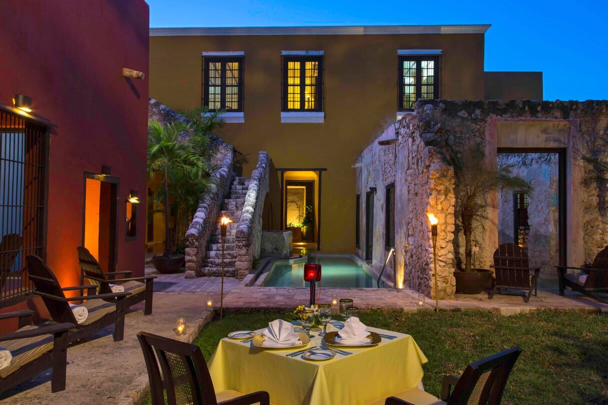 Nighttime courtyard of a restored colonial hacienda in Campeche with stone architecture, private pool, torch lighting, outdoor dining setup with formal table service and lounge seating, ideal for corporate buyouts, incentive travel groups, and exclusive MICE events in Mexico
