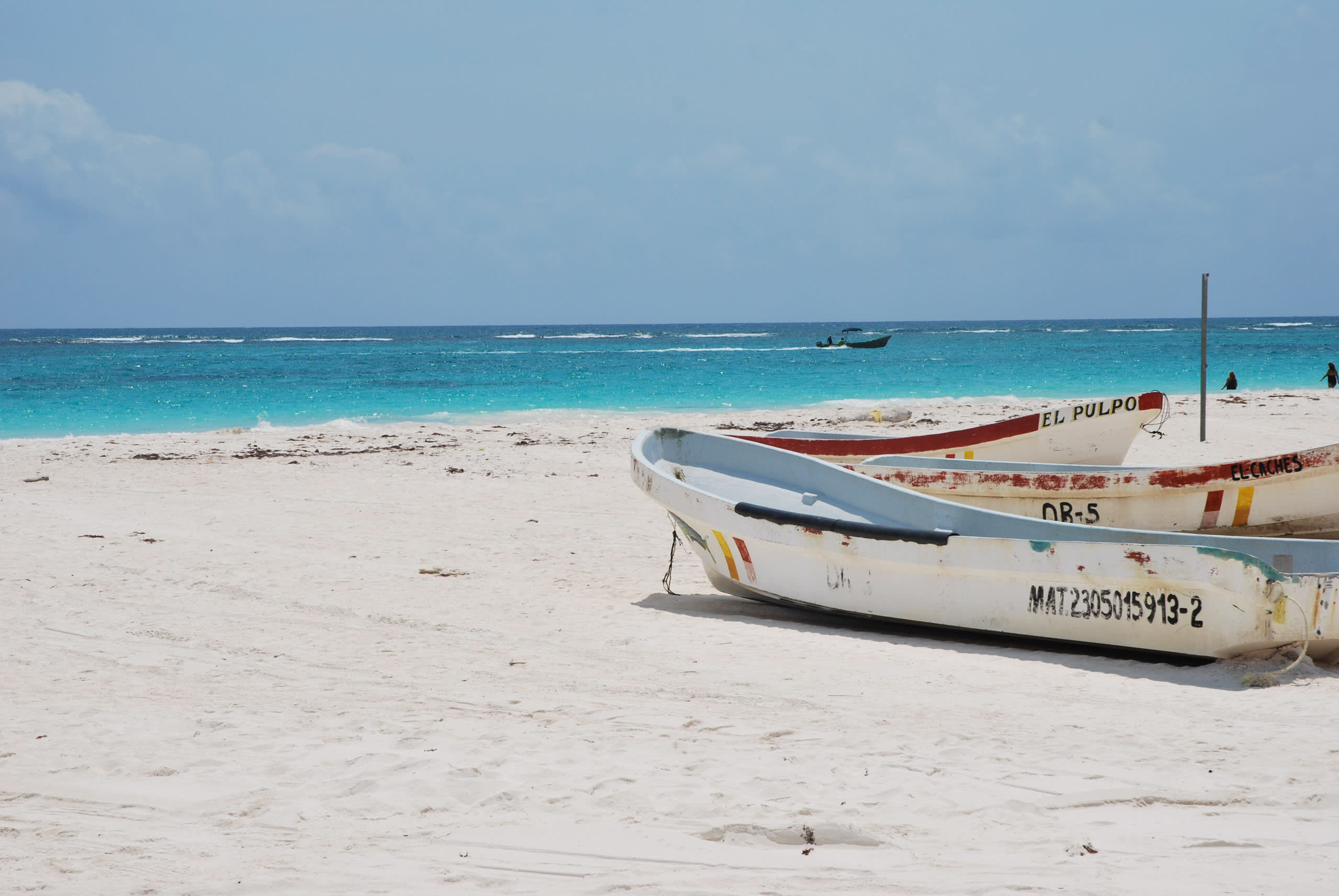 Vibrant turquoise Caribbean waters meet powdery white sands in Tulum, Mexico, where colorful wooden fishing boats rest on the shore, perfect for MICE incentive travel group photos, corporate team-building excursions, and beachfront conference networking events overlooking the azure sea and distant horizon.
