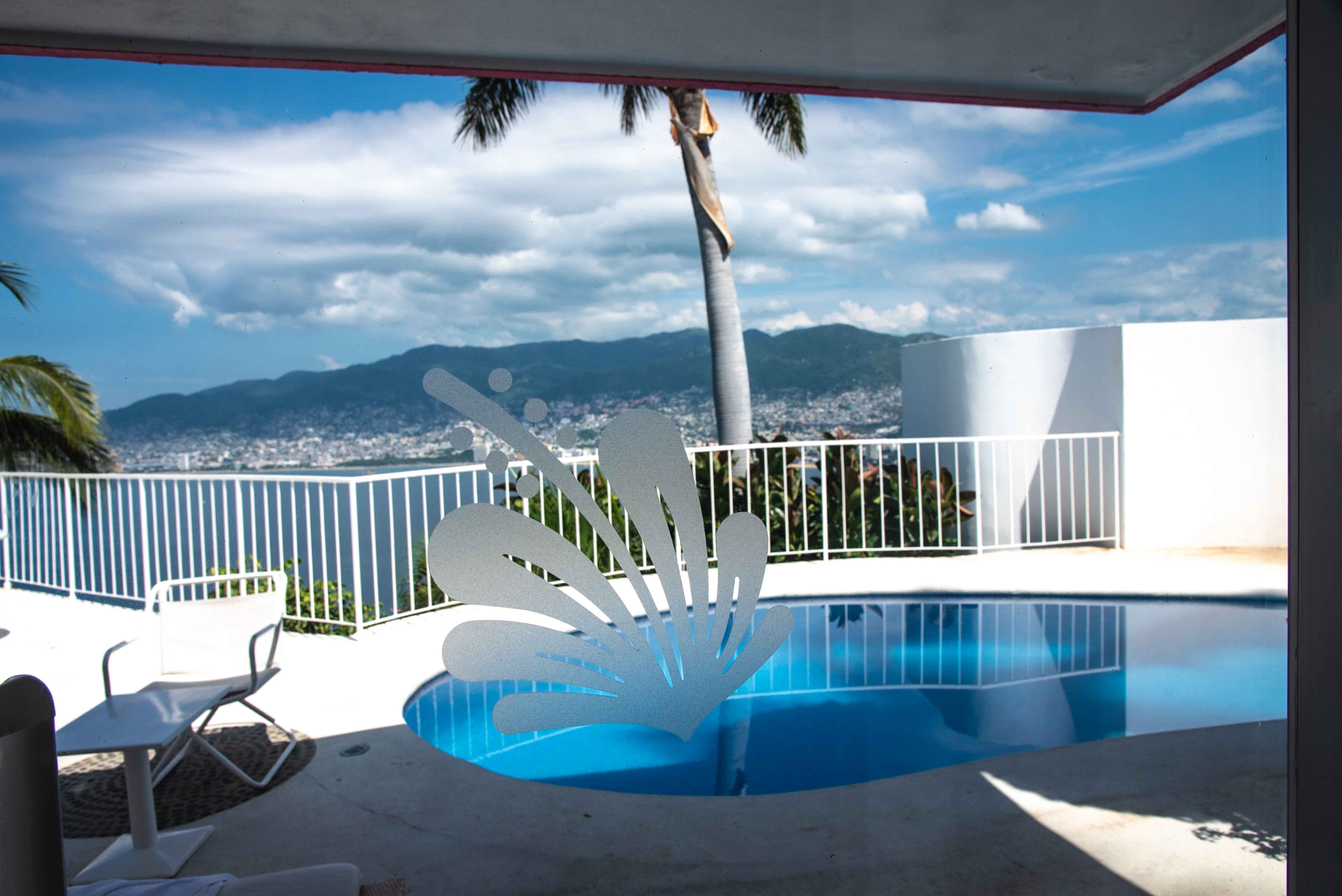A close-up view of a private plunge pool and terrace at Las Brisas Hotel in Acapulco, framed by a decorative glass pane with a splash design. The pool deck overlooks the ocean and city skyline in the distance, confirming the hotel's exclusive setting. This semi-private pool area is a prime feature for incentive travel groups and executive retreats, offering a luxurious and secluded setting for VIP MICE delegates and intimate corporate gatherings.