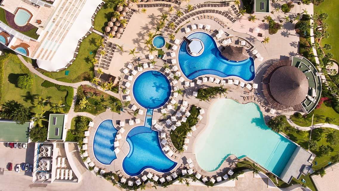  Aerial view of interconnected turquoise swimming pools at a luxury resort in Acapulco, Mexico, surrounded by palm trees, white lounge chairs, umbrellas, and tropical gardens, serving as an ideal MICE venue for meetings, incentives, conferences, exhibitions, and incentive travel programs with relaxing outdoor event spaces.
